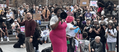 Qween Jean, Organizers for NYC Youth 4 Trans Rights and the action’s ASL interpreter are surrounded by members of the press and participants in the Trans Day of Visibility Rally in Washington Square Park on March 31, 2025. (Photo by Author)